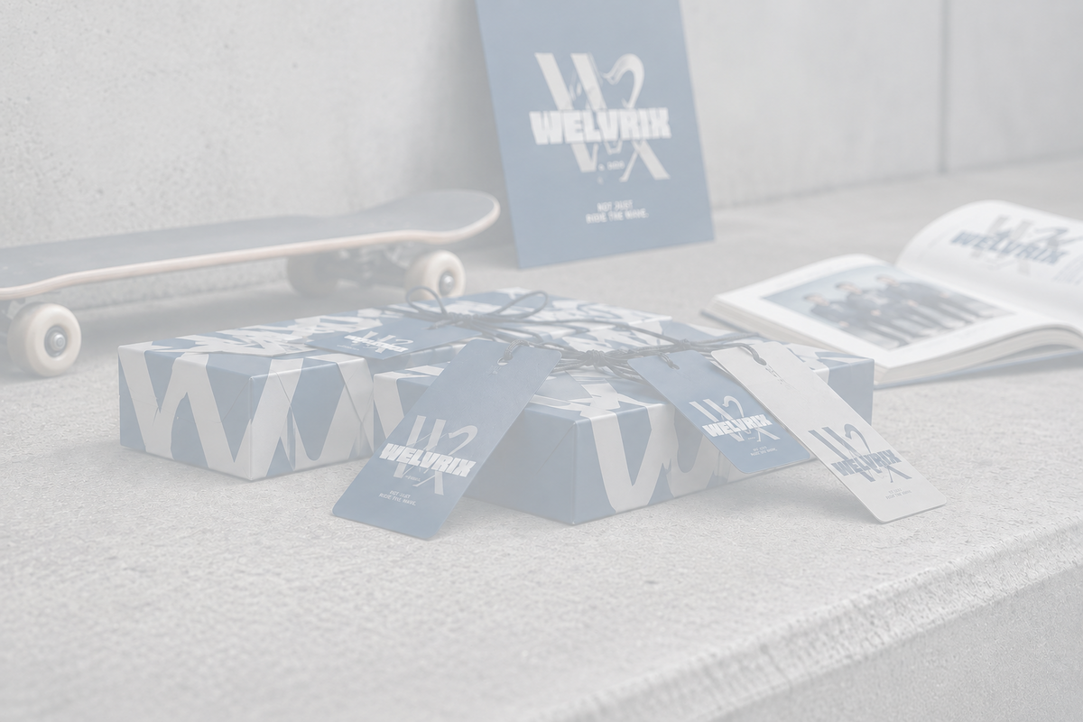 A styled product display featuring navy blue and white branded packaging boxes with matching paper tags, alongside a skateboard, an open magazine, and a standing branded card on a concrete surface.
